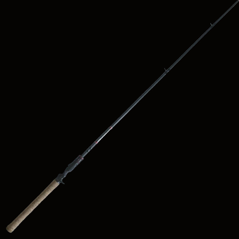 The Keeper Rods-Doozie Doozie 7'6" Pitching/C-Rig Heavy Mod-Fast Precision Casting Rod, featuring a cork handle and black reel seat, lies diagonally on a light surface with wooden planks in the corner.