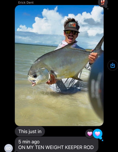 Person holding a large fish by a body of water with a blue sky.