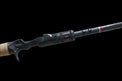 The Doozie Series 73 H+ Frog & Jig Power Casting Rod by Keeper Rods-Doozie is a black rod with a cork handle and red accents. It features an NFC IM intermediate modulus blank for enhanced performance and is displayed on a solid black background, angled from bottom left to top right.